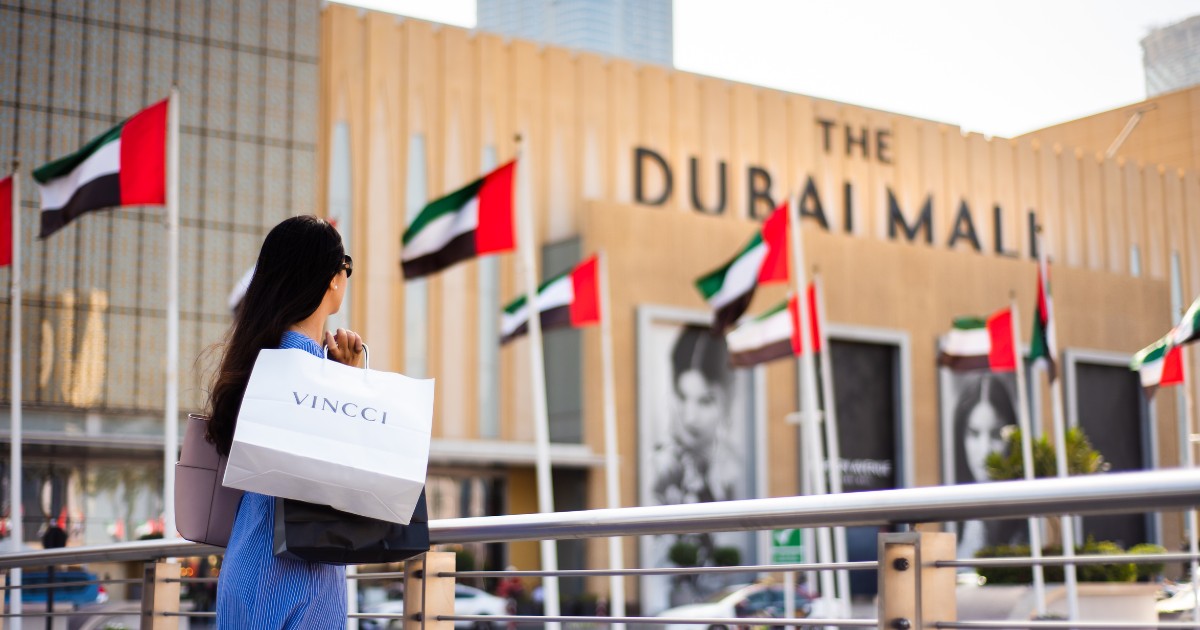Asian tourist in front of Dubai mall main entrance with shopping bags