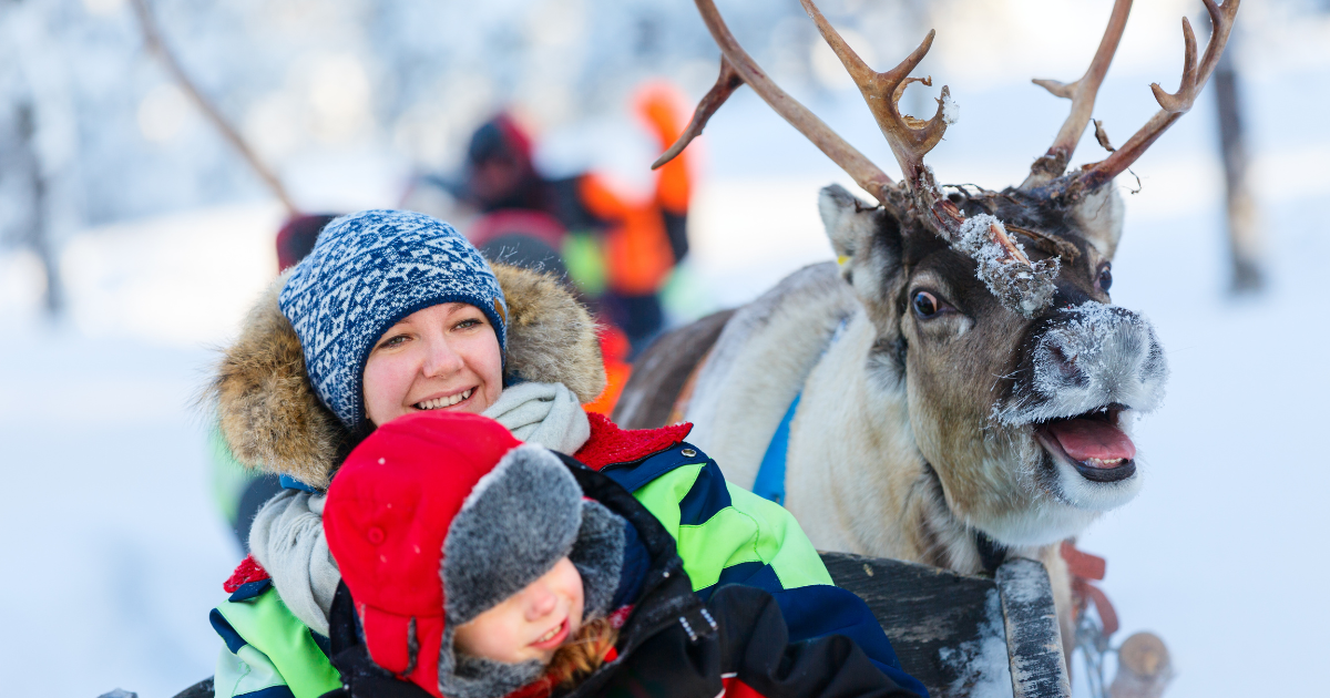Mother and daughter smiling whilst posing next to a reindeer in Lapland, Finland