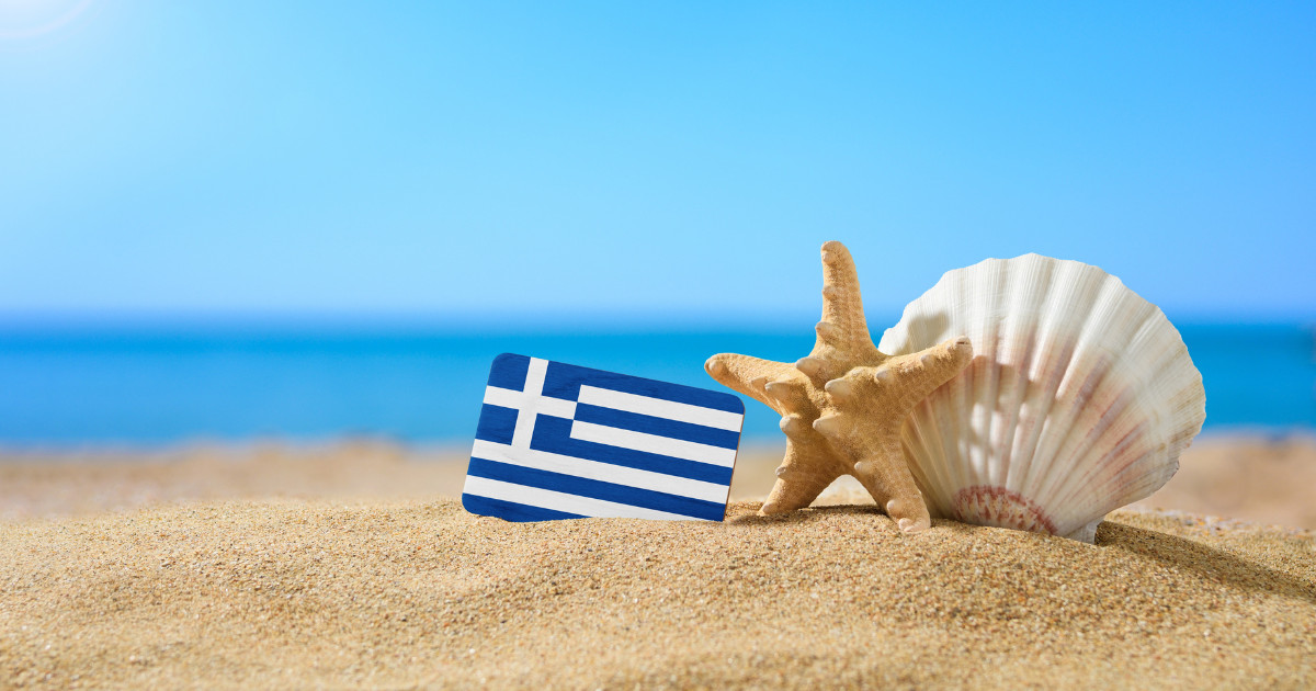 Tropical beach with seashells and Greece flag. The concept of a paradise holiday on the beaches of Greece.