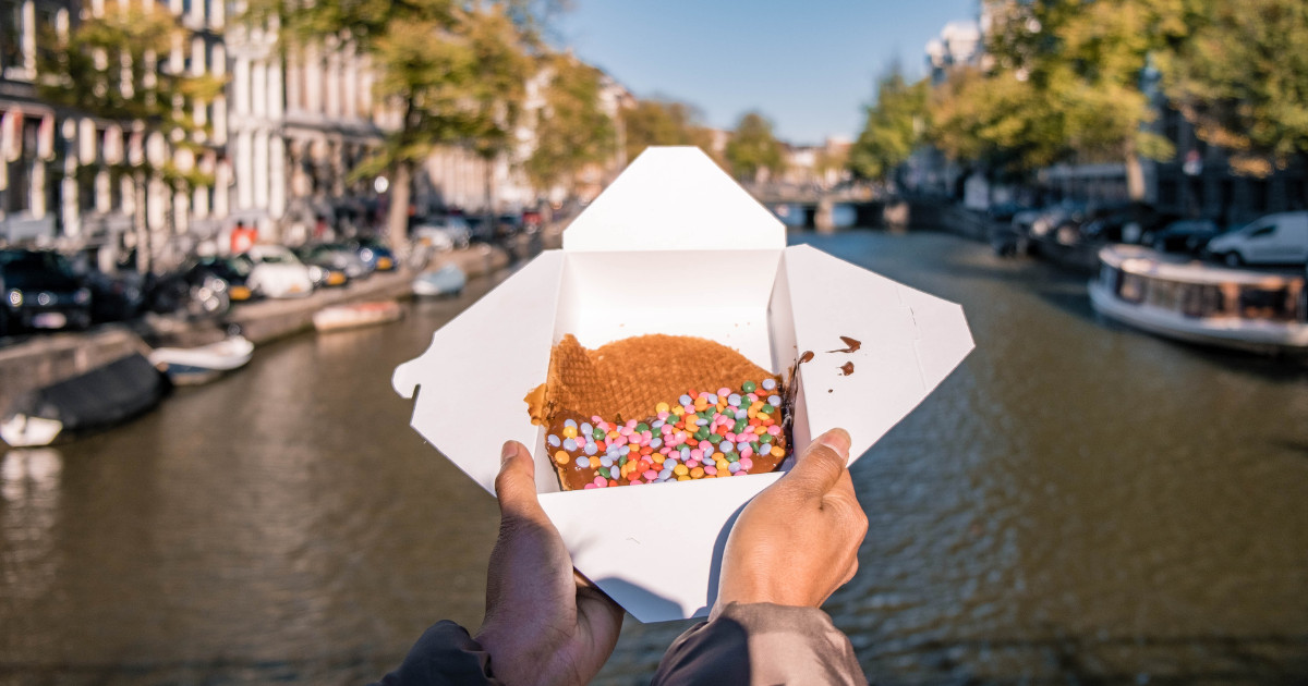 woman hand with Stroopwafel in Amsterdam typical Dutch food. Two circular pieces of waffle filled with caramel-like syrup
